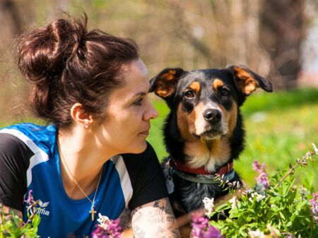 Frau und Hund liegen nebeneinander auf dem Bauch auf einer Wiese
